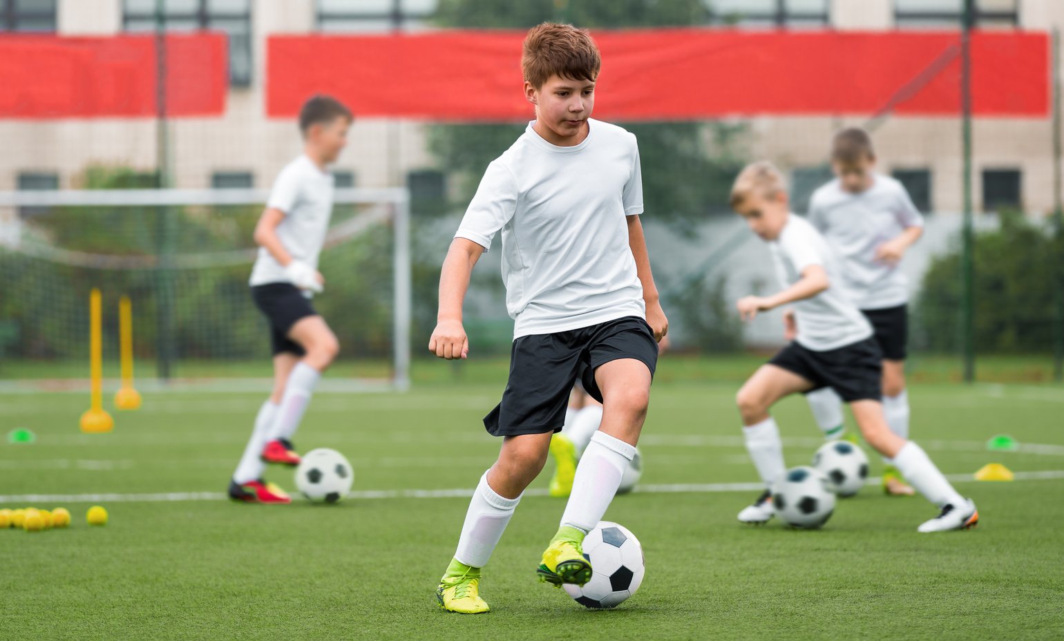 Children kicking soccer balls on artificial grass training field. Young boy leading ball and improving dribbling skills. Physical education class on school training pitch